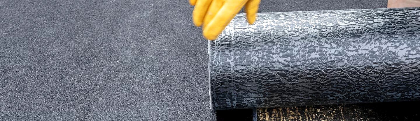 Close-up photograph of a roofer unrolling granule-surfaced modified bitumen roofing membrane