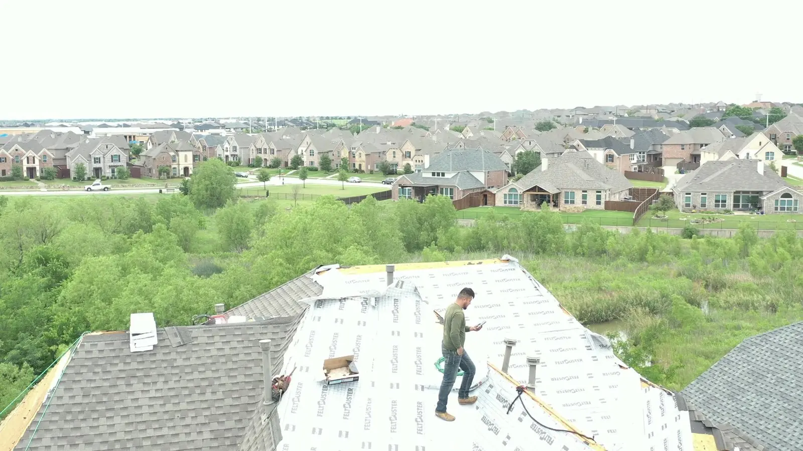 Drone view of a Roofing Giant-managed qualified roofing crew installing a new roof on a Dallas–Fort Worth home, with the neighborhood in the background